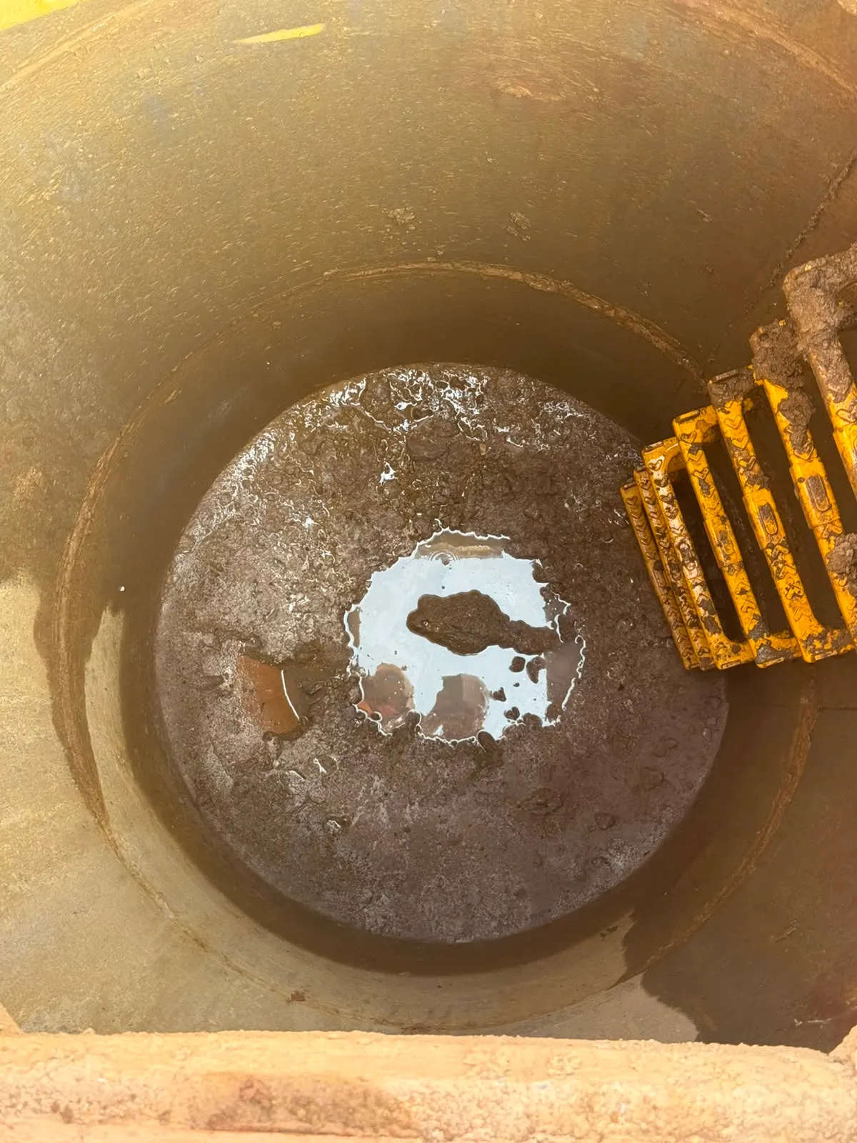 Inside a residential drainage manhole in Northampton showing accumulated silt and debris in the base of the chamber with the step irons visible